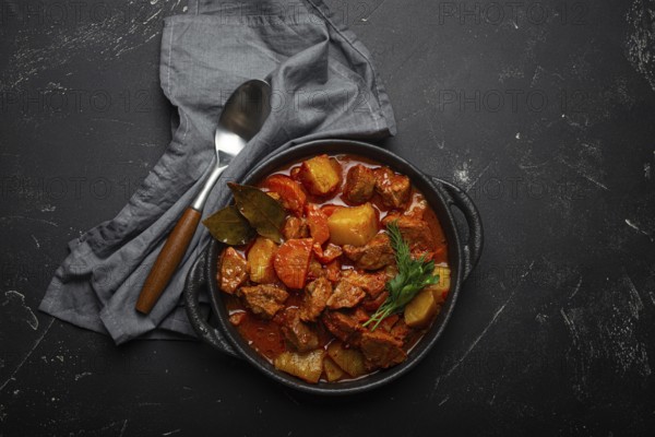 Beef meat stew with potatoes, carrot and delicious gravy in black casserole pot with bay leaves