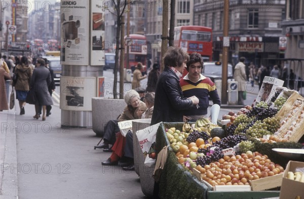 London 1982. A street view of a London street with a stand filled with fruit for sale. Credit