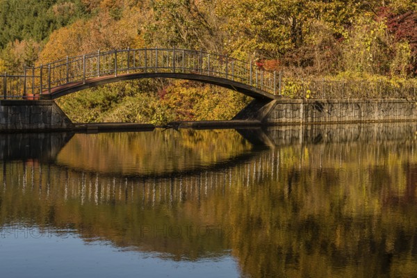 Footbridge over small pond in mountain valley with trees in beautiful fall colors in background,