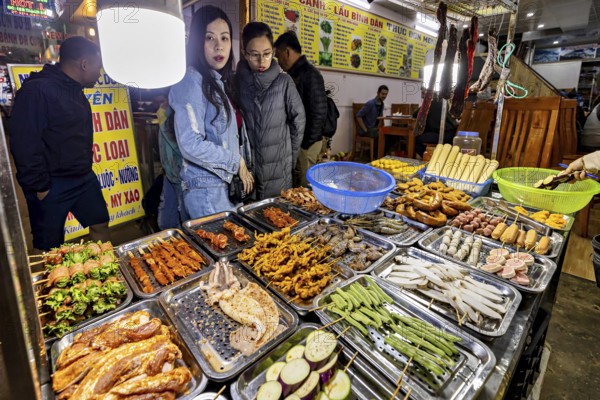 Visitors look at a rich selection of grilled food at a night market, restaurant in the streets of
