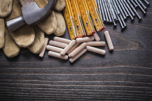Wooden meter heap of dowels claw hammer leather protective gloves and metal nails on vintage wood