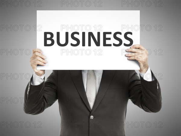A business man holding a paper in front of his face with the word business