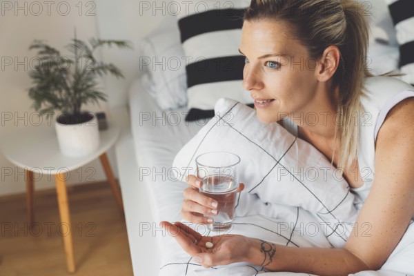 Smiling young caucasian woman taking her morning supplements, vitamin pills with a glass of water