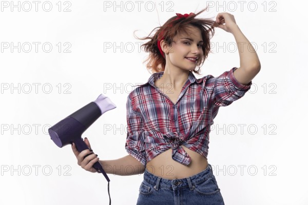 A playful young woman joyfully uses a hair dryer, delighting in her hairstyle with vibrant energy
