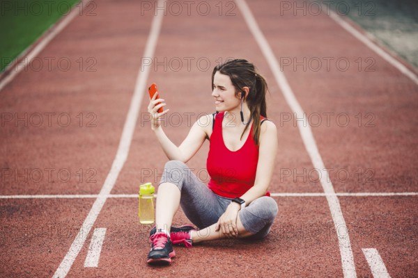 Young woman athlete at the stadium sporting lifestyle, sitting on the track, taking selfie photo on