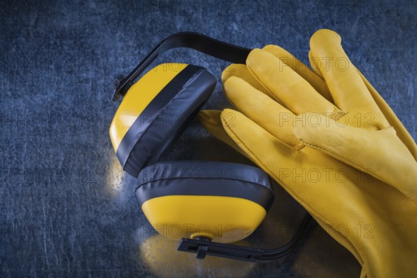 Safety yellow earmuffs and leather construction gloves on scratched metallic surface building