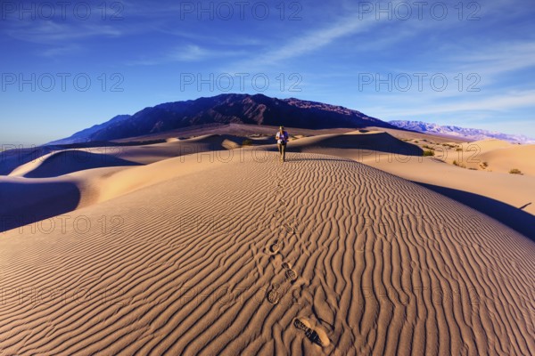 Sunrise in the orange sands of the desert Mesquite Flat, USA. Woman - photographer is among the