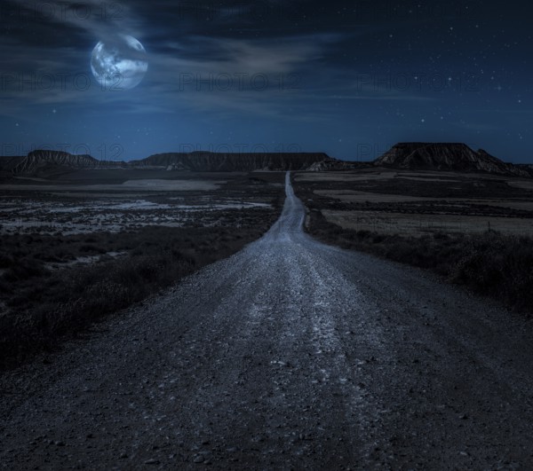 Moon, stars and clouds in the night. Wild west road illuminated from the moon. Moonlight and road