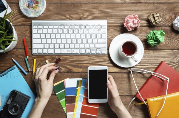 Web designer choosing colors from swatches at wooden desk. Top view office workplace with computer