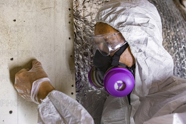 A man wearing protective breathing equipment is viewed closeup, inspecting signs of mold and mildew