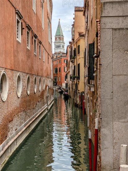 Narrow Venetian canal flanked by historic buildings with the bell tower in the distance. Venice,