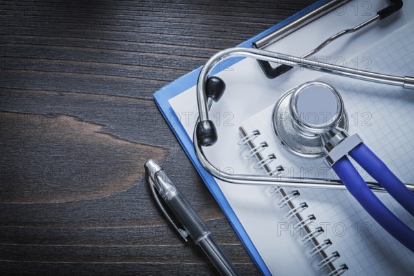 Clip board squared notepad pen and medical stethoscope tablet on vintage wooden background medicine