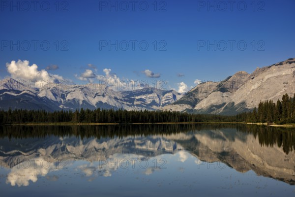 The Canadian Rockies and bright blue sky are reflected in a lake near Canmore, Alberta, Canada,
