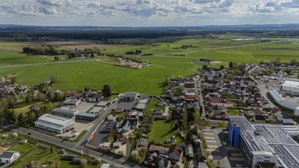 Aerial view of a village with surrounding fields and country road under a cloudy sky, Mitterteich,