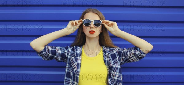 Portrait of modern stylish young woman in white glasses, casual clothing posing on blue wall