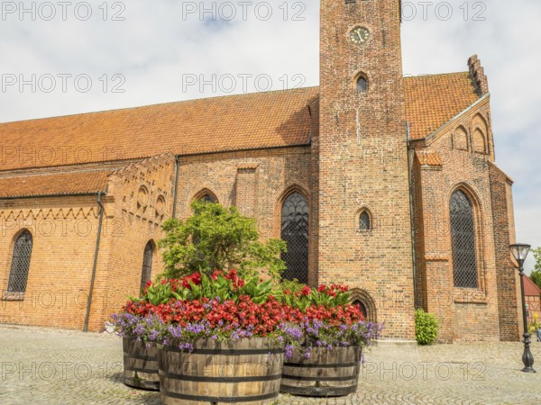 Church in the background with large flower pots in the foreground, historic brick walls, ystad,