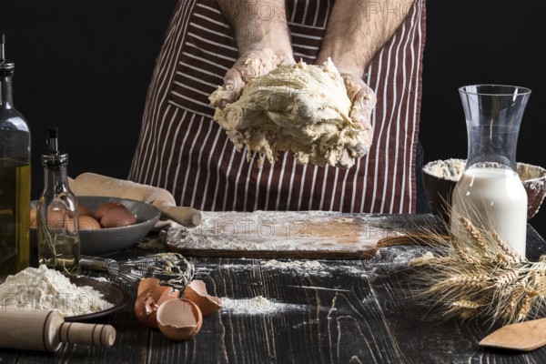 A handful of flour with egg on a rustic kitchen. Against the background of men's hands knead the