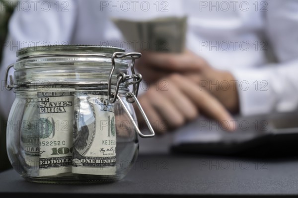 Dollar Banknote Saving Money In Glass Jar. Unrecognizable man calculate money on calculator