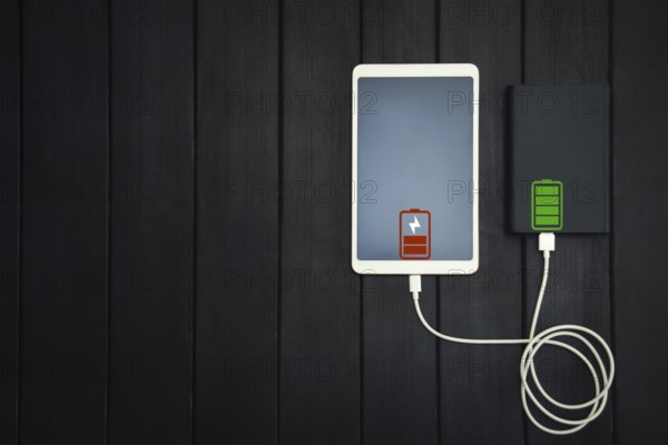 Power bank loads tablet PC, smartphone, isolated on wooden background. charging concept. free