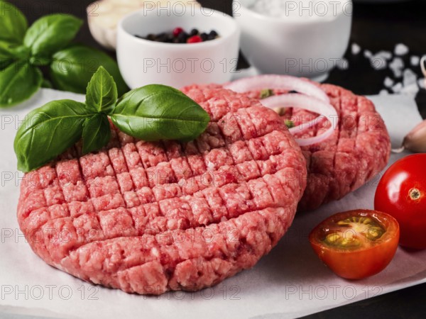 Close up view of two raw meat steak cutlets for burger with vegetables, spices and fresh basil.