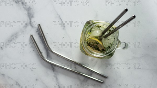 Metal drinking straws and cold drink in glass mason jar on white marble background. Top view or