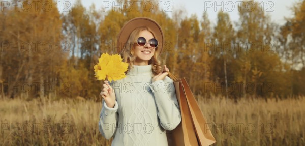 Autumn portrait of stylish happy young woman with shopping bag and maple yellow leaves, fashionable