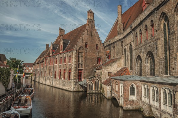 Old buildings on the canal bank, boats and sunny blue sky in Bruges. With many canals and old