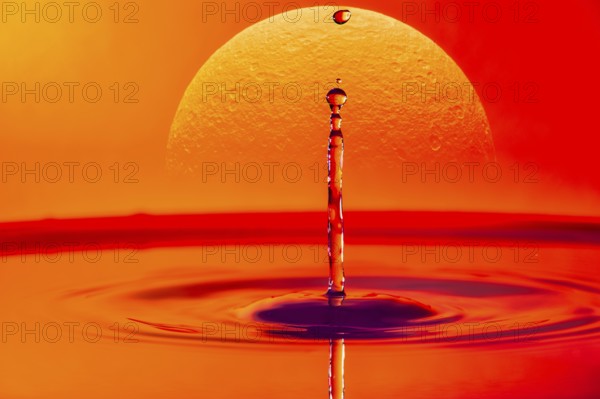 A single drop of water falling into a body of water with a glowing sunset in the background,