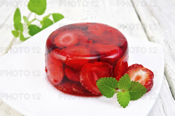 Strawberry jelly with mint and berries in a plate on a kitchen towel on the background light wooden