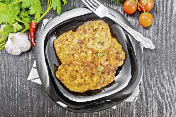 Fritters of minced meat in a plate with a fork on napkin, garlic, parsley and hot pepper on black
