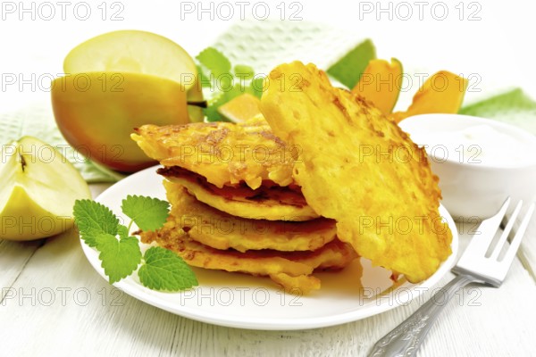 Pumpkin and apple fritters in a white plate, sour cream in a bowl, napkin, mint and fork on wooden