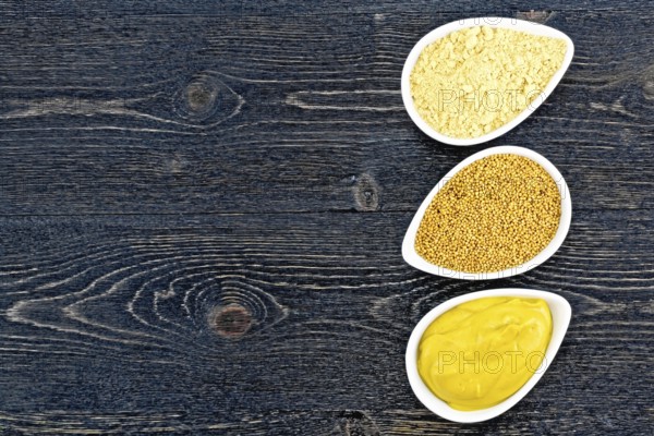 Mustard sauce, seeds and mustard powder in three saucepans on the background of a black wooden