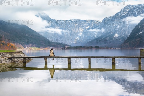 Woman sitting on a wooden bridge over the lake Hallstatter, admiring the peaks of the Austrian Alps