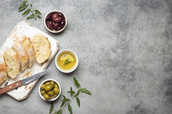 Sliced fresh ciabatta on cutting kitchen board, green and brown olives, olive oil with rosemary,