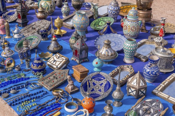 A colorful Moroccan market scene along a bustling street, with vendors selling spices, textiles,
