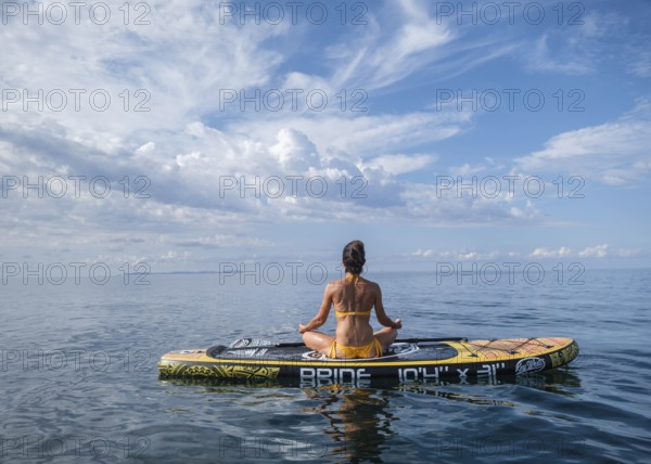Woman practicing yoga on a surfboard under a dramatic sky, Estalella, coast of Llucmajor, Majorca,