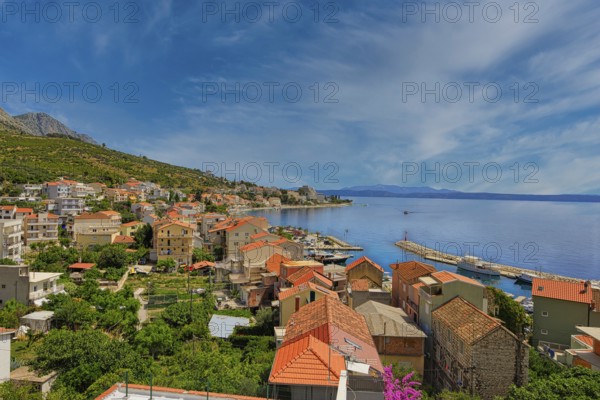 Coastal town with red roofs and views of the sea and distant mountains under a blue sky, Makarska