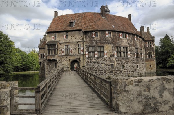 Wide bridge leads to a historic castle with moat, surrounded by nature, cloudy sky, lüdinghausen,