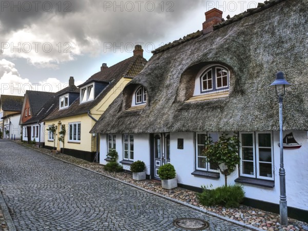 Traditional houses with thatched roofs and cobblestone streets under a cloudy sky, maasholm,