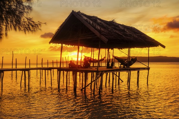Native people relaxing in hammocks on wooden jetty during sunset on Kri island, Raja Ampat, West