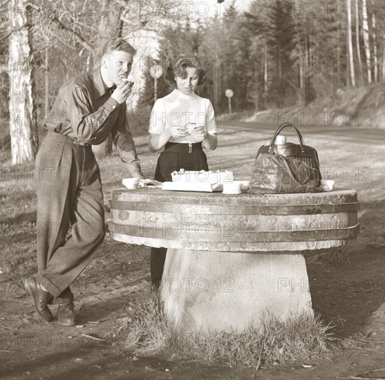 Lifestyle in the 1950s. A young couple has stopped to have a coffee and a sandwich by the roadside.