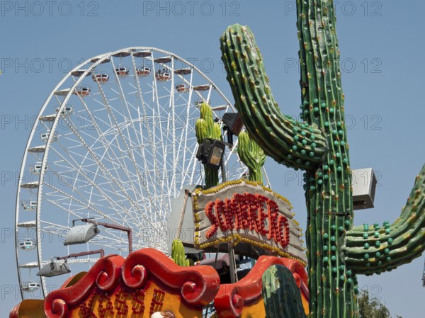 Colourful amusement park with a large Ferris wheel and decorative cacti under a clear sky, Vienna,