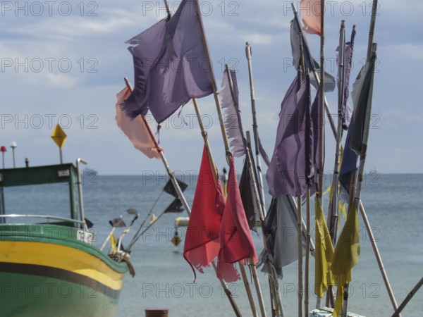 Colourful flags waving in the wind, next to a green boat in front of a wide sea and blue sky,