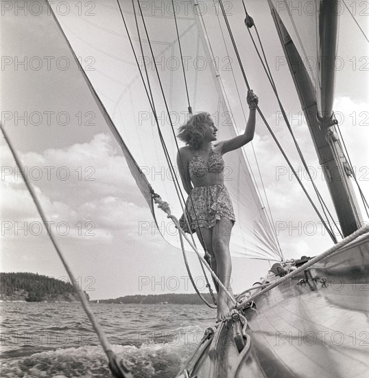 1940s sailing boat. A young woman is aboard a fashionable sailing boat and is standing on deck when