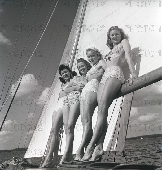 1940s sailing boat. Four young women are standing and leaning against the sails of the boat and