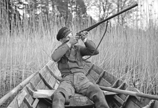 In the 1930s. A man sits in a rowing boat and aims his rifle upwards to shoot ducks. Sweden 1939.