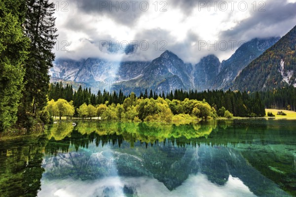 The sun's rays break through the clouds. The smooth surface of the water reflects forest and