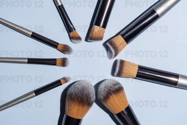 Make up brush sets arranged in a circle on blue background, top view with copy space. Cosmetics