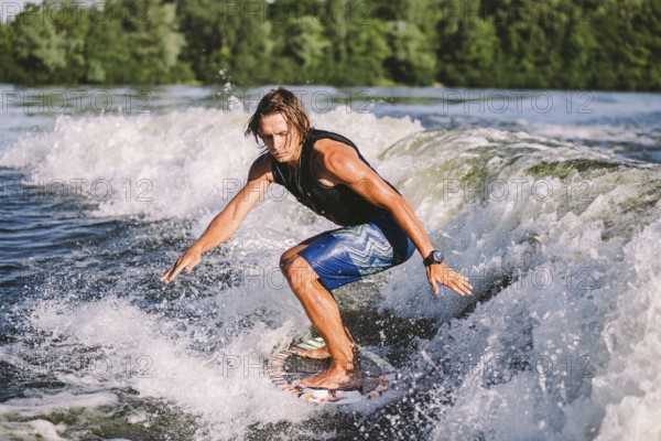 Young athletic man with long hair wakesurfing on waves of river in sunny summer weather. Ttheme