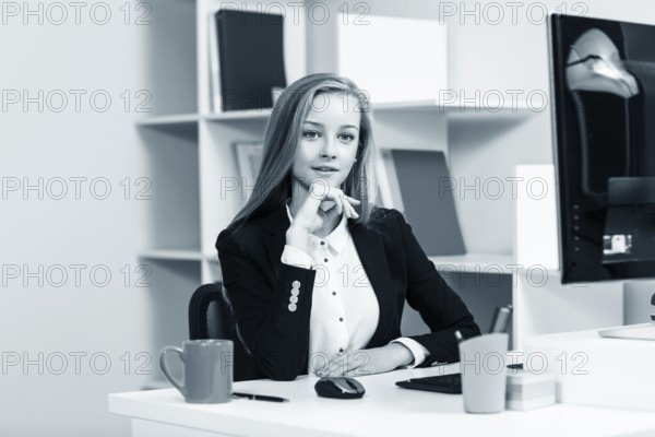 Young pretty business woman sitting at the desk with computer in blue office